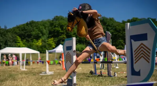 Dziewczynka na kucyku z patyka przeskakuje przez przeszkodę. Czy hobby horse to sport? Z pewnością wymaga zwinności i determinacji!