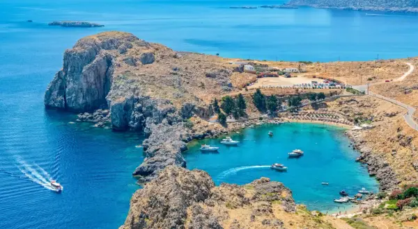 Malownicza zatoka na Rodos, idealna do zwiedzania samochodem. Woda krystalicznie czysta, plaża pełna ludzi, a wokół skaliste wybrzeże.
