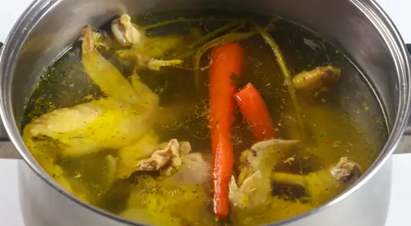 Gotowanie rosołu pod przykryciem to sekret głębokiego smaku. Widać kawałki kurczaka, marchewkę i przyprawy w bulionie.