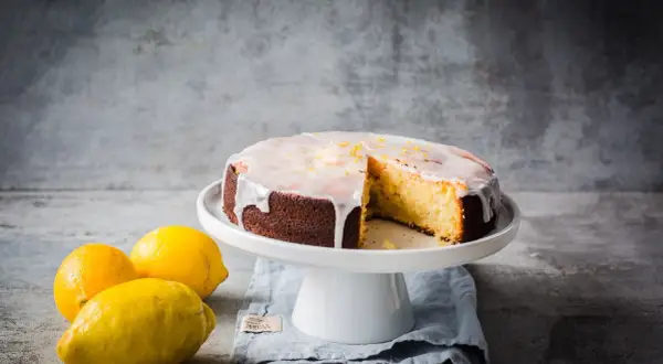 Ein saftiger zitronenkuchen mit Zuckerguss und Zitronenschale, daneben frische Zitronen.
