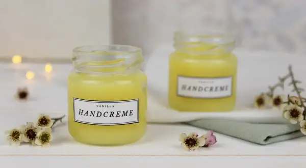 Zwei Gläser mit selbstgemachter Handcreme, verziert mit kleinen Blüten. Perfekt zum Handcreme selber machen für Kinder.
