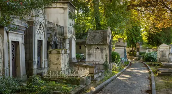 Allée pavée dans un cimetière verdoyant, bordée de mausolées. Idéal pour un modèle de lettre pour renouvellement de concession cimetière.