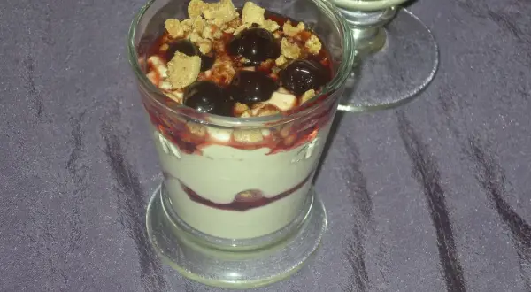 Dessert im Glas mit Kirschen, zerbröseltem Keks und Fruchtsauce.