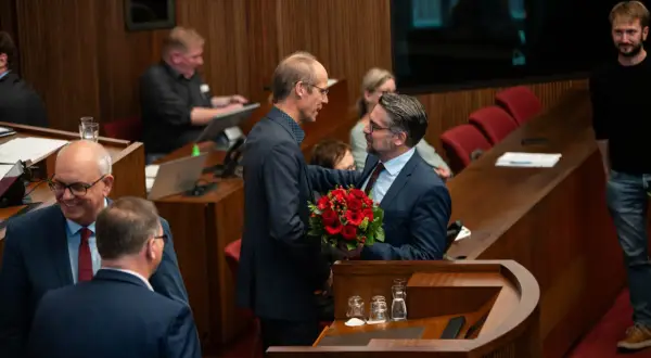 Ein Mann überreicht Mark Rackles einen Blumenstrauß in einem Sitzungssaal.