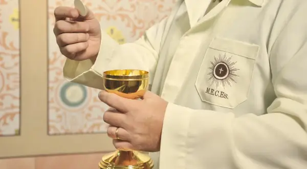 Dłoń trzymająca hostię i złoty kielich podczas ceremonii religijnej.