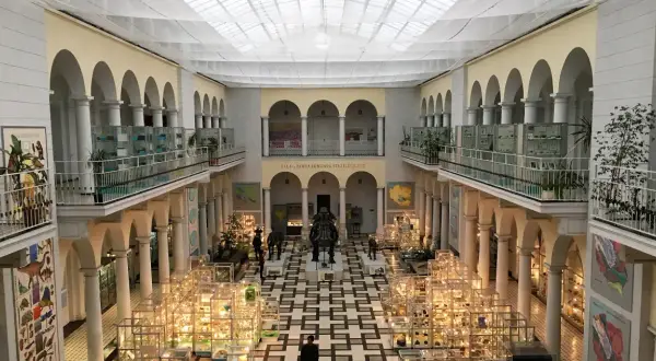 Wnętrze muzeum sztuki w Polsce z gablotami pełnymi eksponatów, rzeźbami i arkadami.