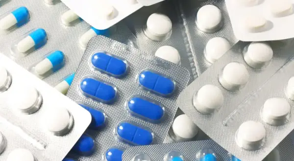 Blistry z białymi i niebiesko-białymi kapsułkami oraz okrągłymi białymi tabletkami, jak polopiryna.