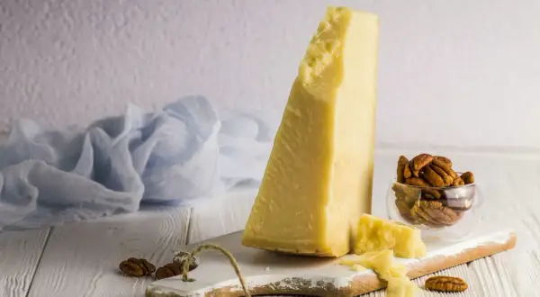Kawałek sera Grana Padano, czy to parmezan? Obok orzechy pekan i błękitna tkanina.