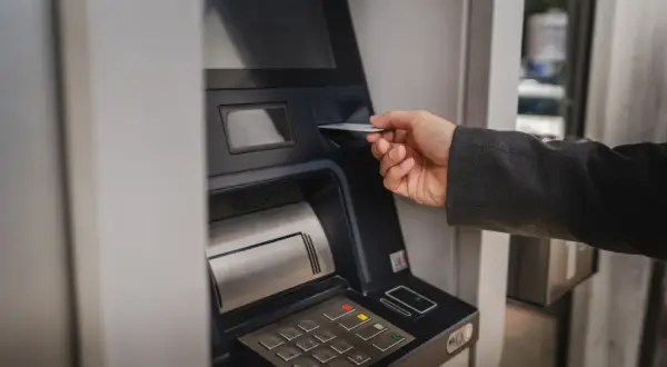 Dłoń wsuwa kartę do bankomatu, by sprawdzić, ile można wypłacić.