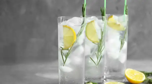 Trzy orzeźwiające gin fizz z lodem, plasterkami cytryny i gałązkami rozmarynu, ozdobione zielonymi słomkami.