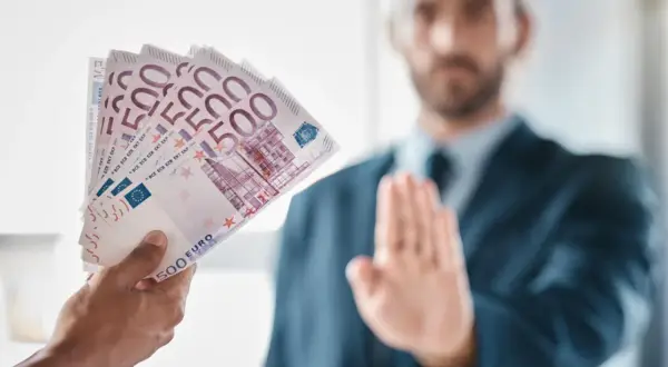 Ręka podaje plik banknotów 500 euro, mężczyzna w garniturze odrzuca je, co może symbolizować pozew o zapłatę.