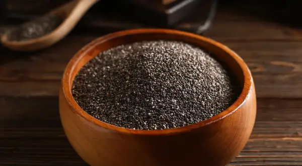 Nasiona chia jak jeść? W drewnianej misce pełnej drobnych, czarnych ziarenek. Idealne do dodania do jogurtu, owsianki czy smoothie.
