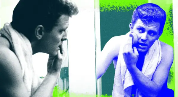 Visage homme 40 ans, se regardant dans le miroir, une serviette sur les épaules, appliquant un produit sur sa peau.