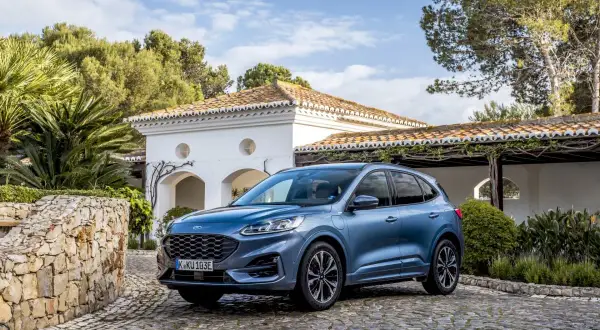Niebieski Ford SUV Kuga, jeden z popularnych ford suv modele, zaparkowany na brukowanym podjeździe przed białym domem z czerwoną dachówką.