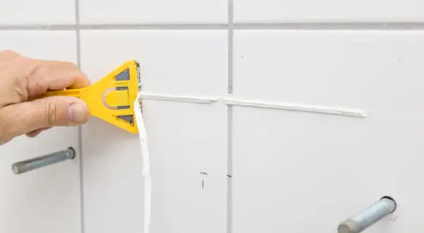Main jaune en action pour enlever silicone vinaigre. Le joint est retiré proprement.
