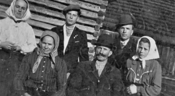 Famille posant devant une maison en bois. Les femmes portent des foulards, les hommes des chapeaux. Un nom de famille slovaque pourrait être associé à cette photo d'ancêtres.