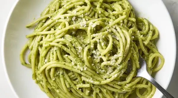 Pyszny makaron z pesto, posypany parmezanem, czeka na widelcu. Idealny na szybki obiad.