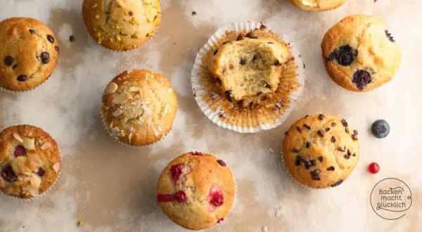 Verschiedene Muffins, die nach einem Muffins Grundrezept gebacken wurden: mit Schokostückchen, Blaubeeren, Himbeeren und Mandeln. Einer ist angeknabbert.