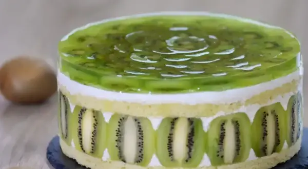 Tort z galaretką kiwi i plasterkami kiwi na bokach.