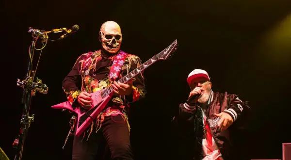 Muzyk w masce czaszki gra na różowej gitarze, wokalista w czapce śpiewa na scenie podczas impact festival.