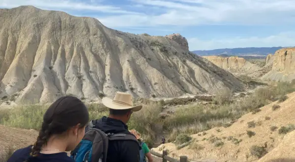 Senderos para visitar el desierto de Tabernas gratis. Familias exploran paisajes áridos bajo un cielo azul con nubes.