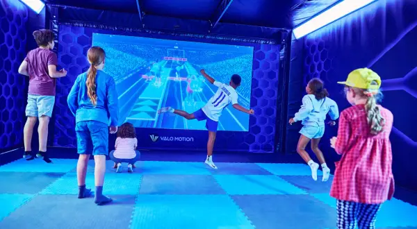 Kinder haben Spaß bei interaktiven Veranstaltungen in Berlin. Sie springen und spielen vor einer großen Leinwand mit einem Fußballspiel.