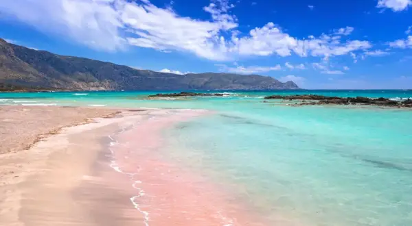 Różowa plaża z turkusową wodą i górami w tle – to jedna z najpiękniejszych plaż na świecie.