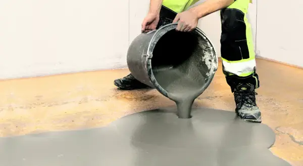 Arbetare häller jordfuktad betong från en hink för att jämna ut ett golv.
