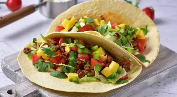 Dwa tacos z mielonym mięsem, pomidorami, papryką, mango i kolendrą na desce.