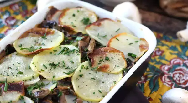 Zapiekanka ziemniaczana z pieczarkami, posypana szczypiorkiem, w białym naczyniu.