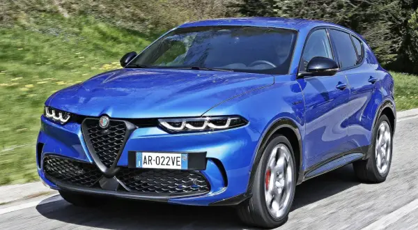 Niebieski SUV marki Alfa Romeo pędzi po asfaltowej drodze, otoczony zielenią.