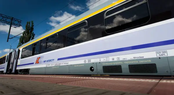 Pociąg Heweliusz PKP Intercity z Wrocławia, z widocznymi zbiornikami powietrza i klimatyzacją, na tle błękitnego nieba z chmurami.
