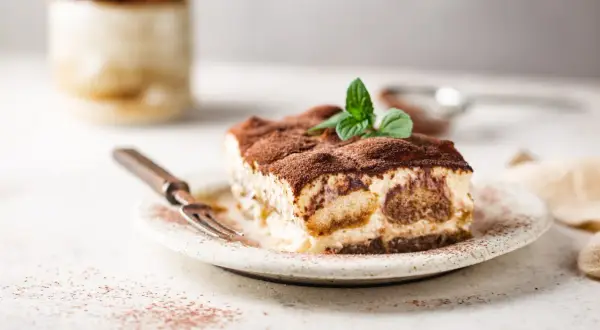 Une part de tiramisu onctueux, saupoudrée de cacao, garnie de menthe fraîche. Parfait pour une recette tiramisu réussie.