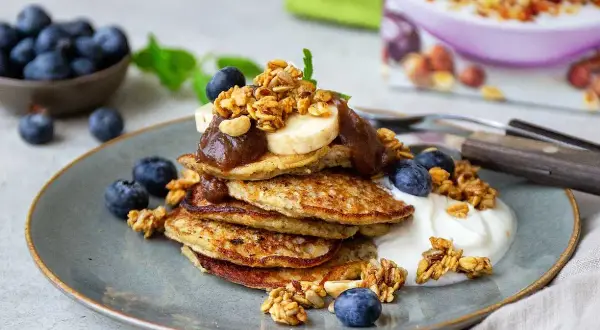 En hög med bananpannkakor toppas med banan, sylt och granola. Ett perfekt bananpannkaka recept för en lyxig frukost eller brunch.