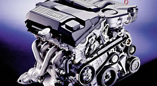 Silnik BMW M52B20, z charakterystycznym napisem BMW na pokrywie zaworów, prezentuje skomplikowaną konstrukcję z widocznymi kolektorami wydechowymi i paskiem napędowym.