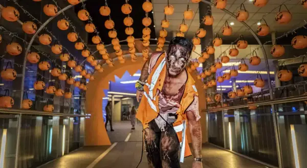 Un espeluznante zombie con maquillaje de Halloween avanza bajo un arco decorado con calabazas en Puerto Venecia.