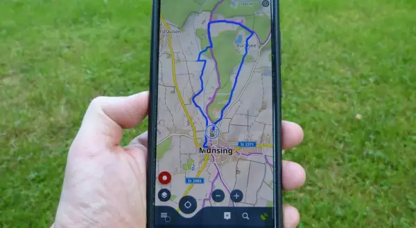 Hand hält Smartphone mit einer Wanderwege App, die eine Route bei Munsing anzeigt. Perfekt für die nächste Tour!