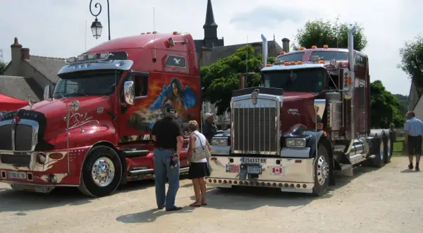 Deux camions américains tuning, l'un rouge vif avec une peinture personnalisée, l'autre bordeaux, se dressent fièrement.