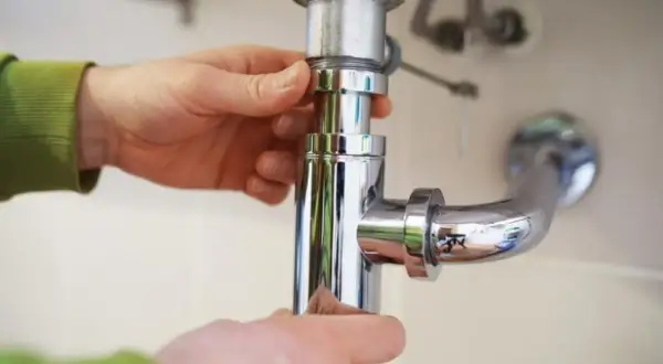 Mains pour démonter un siphon de lavabo, une étape clé pour savoir comment déboucher.