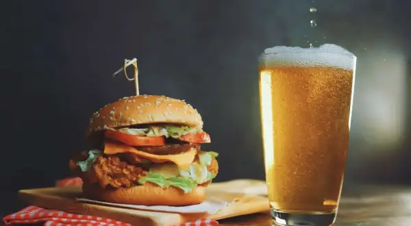 Un succulento hamburger con formaggio fuso e lattuga, accompagnato da una birra bionda spumeggiante.