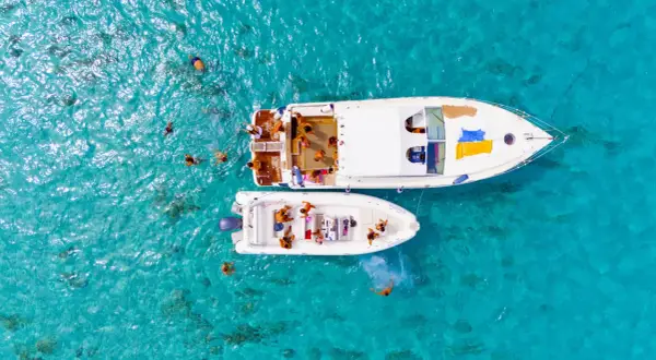 Gente si gode il mare di Favignana, nuotando e rilassandosi su due barche in acque cristalline.