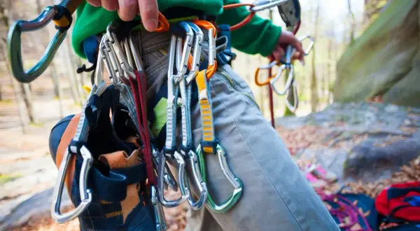 Kletterer mit Ausrüstung für trad climbing, darunter Kletterschuhe und Karabiner, bereit für den Aufstieg.