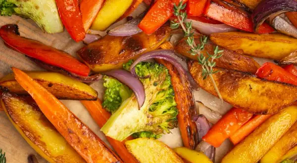 Un assortiment coloré de légumes rotis au four : carottes, pommes de terre, brocolis et oignons rouges, parsemés de thym frais.