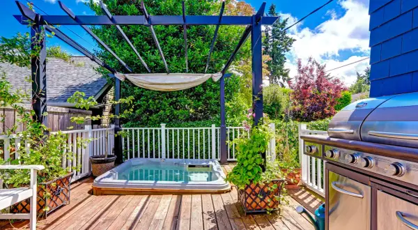 Un coin jacuzzi extérieur sous une pergola, avec un barbecue à proximité, invite à la détente.