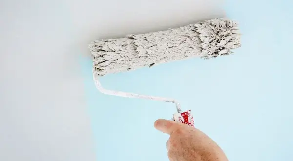 Main d'un peintre utilisant un rouleau pour appliquer une peinture bleu pâle sur un mur. Quel rouleau pour peinture velours !