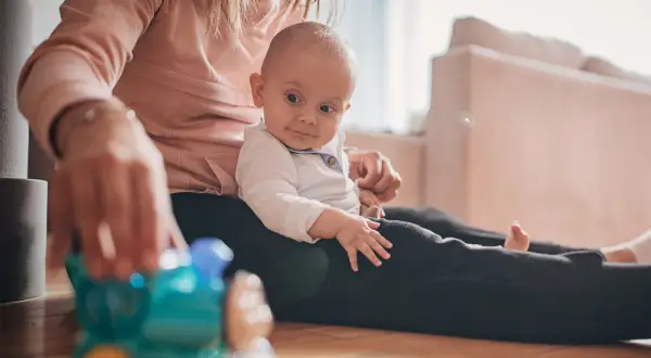 Mama bawi się z 9-miesięcznym dzieckiem, które siedzi na jej kolanach. Przed nimi leży zabawkowy pociąg.