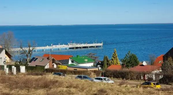 Widok na morze i molo w Mechelinkach. Domy z czerwonymi i zielonymi dachami, samochody na drodze. Mechelinki atrakcje to spacer po molo i podziwianie krajobrazu.
