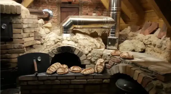 Frisches Brot wird im Pizzaofen gebacken. Mehrere Laibe liegen bereit, einige sind schon im Ofen.