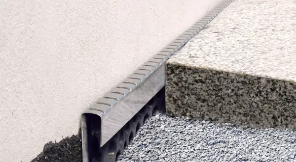 Noppenbahn mit Bitumen kleben: Detailaufnahme einer Fassadenabdichtung mit Drainageschicht und Granitstufe.