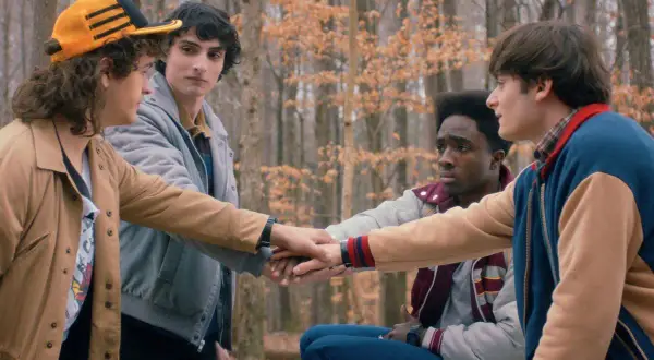 Czterech przyjaciół z Stranger Things w lesie, łączących dłonie.